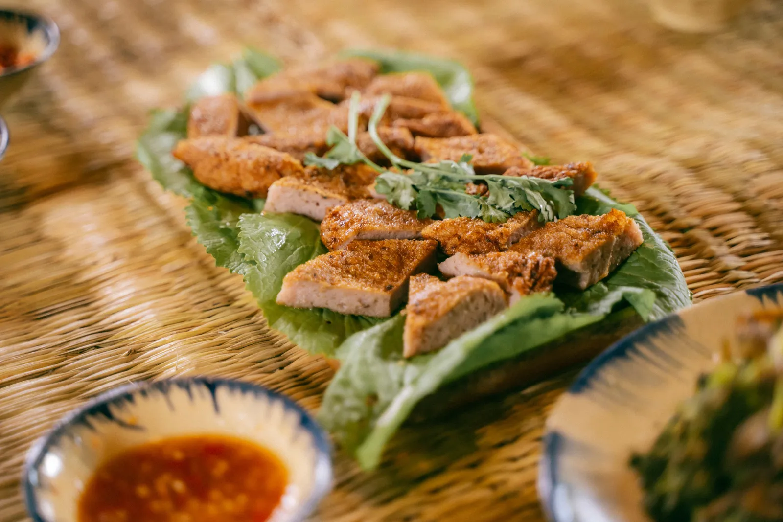 Slices of crispy Balinese roast pork belly served on a platter with fresh leaves