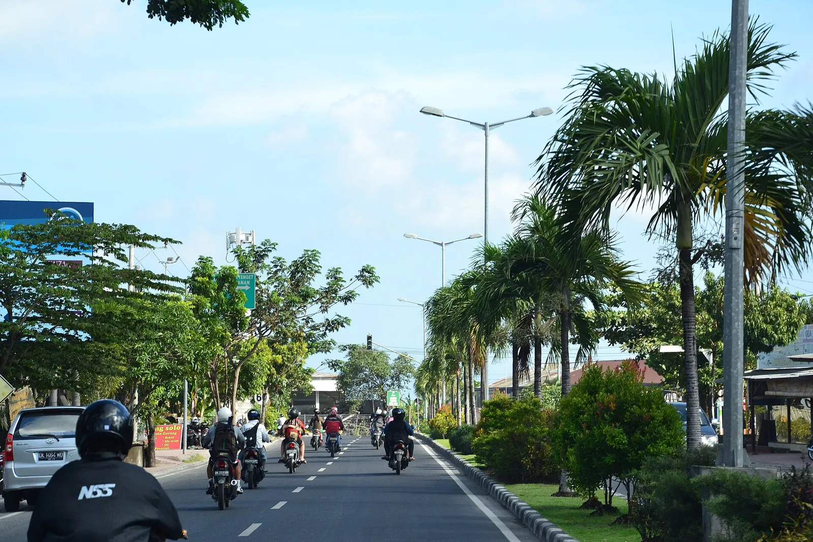 Scooters and cars on a palm-lined main road in southern Bali on a sunny day