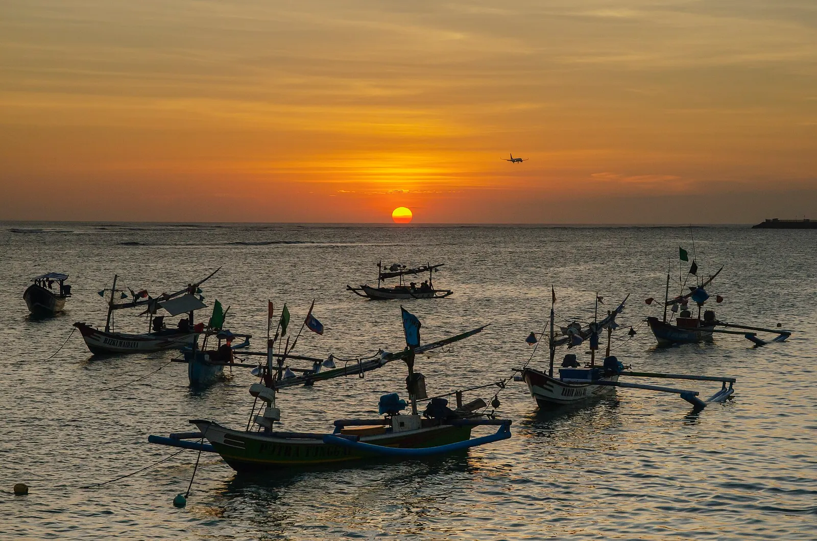 Traditional fishing boats at sunset near Bali airport with a plane on final approach