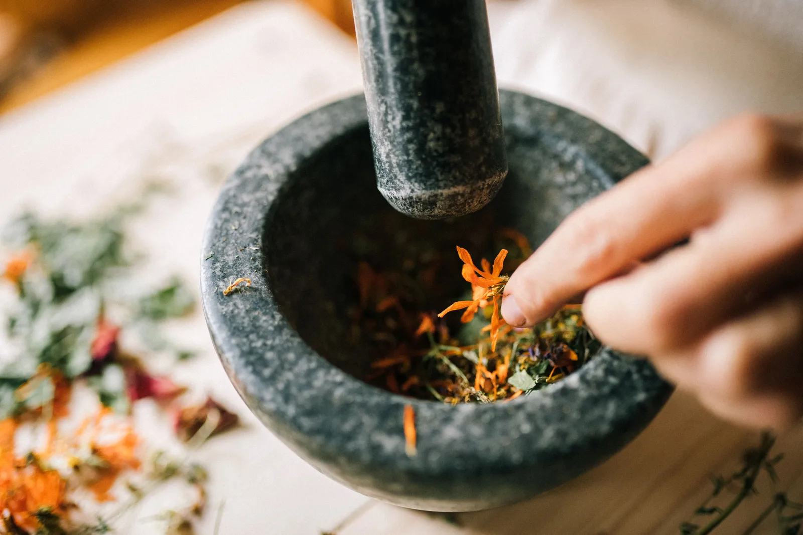 Hands grinding spices with a stone mortar and pestle at a Balinese cooking class, with fresh ingredients laid out, Indonesia