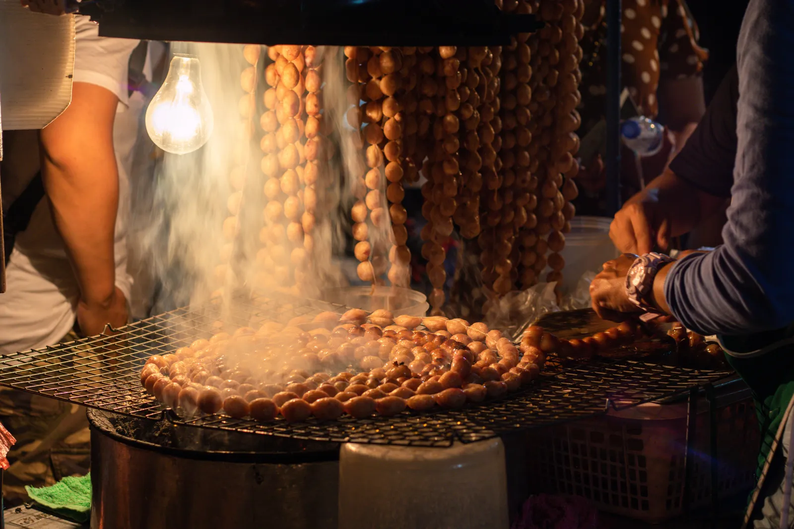 Food stalls with grills and hanging lights at a busy night market in Gianyar, Bali