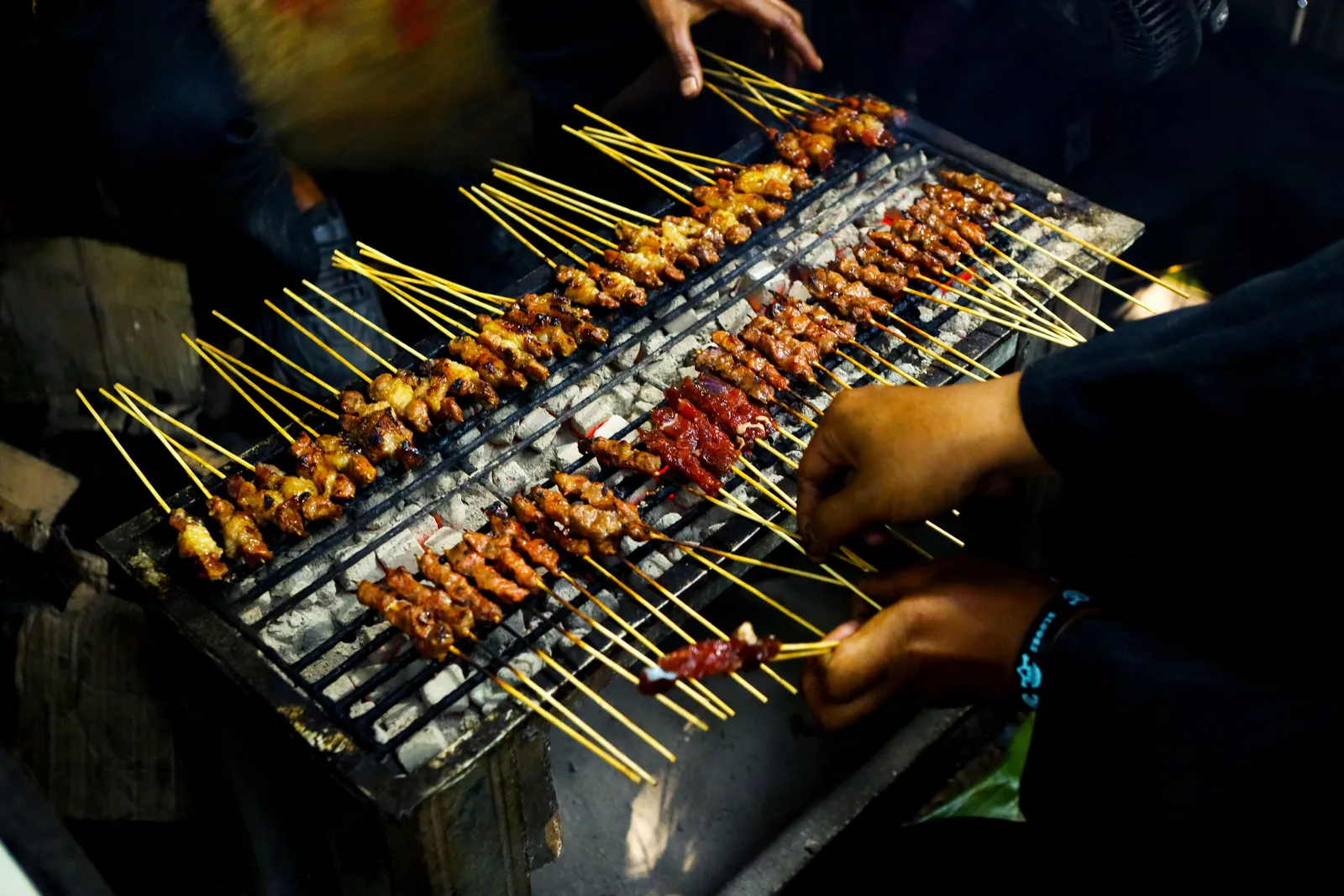 Skewers of chicken satay grilling over charcoal at a Balinese night market stall