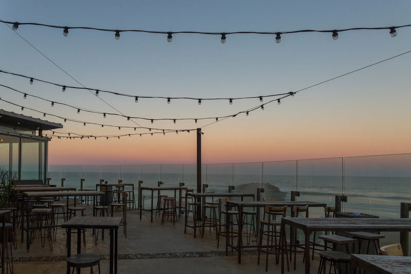 a rooftop cocktail bar terrace at dusk in Bali with low lighting and the sea beyond