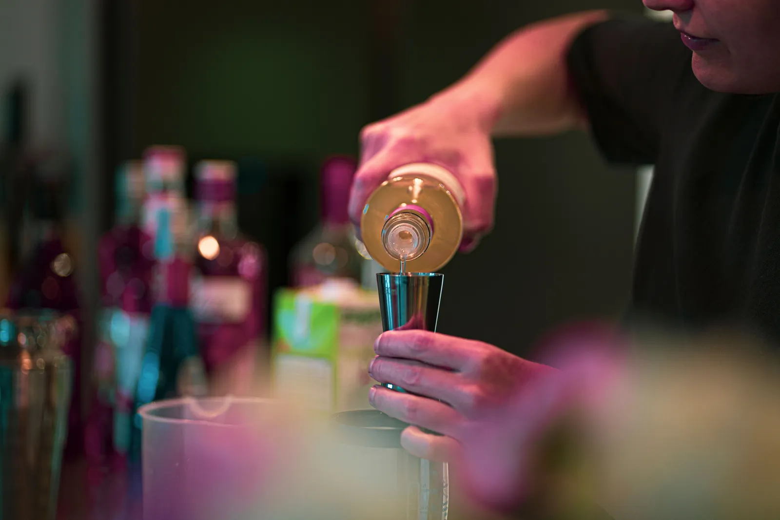 A bartender pouring from a sealed branded spirit bottle at a lit bar counter in Seminyak, Bali at night