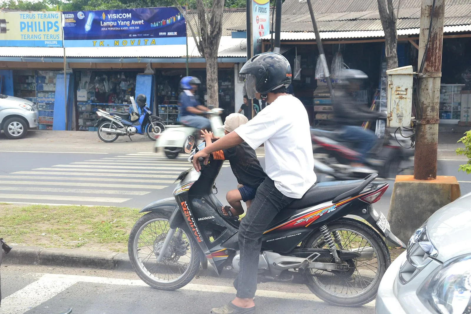 A helmeted rider on a scooter in daytime street traffic in Bali