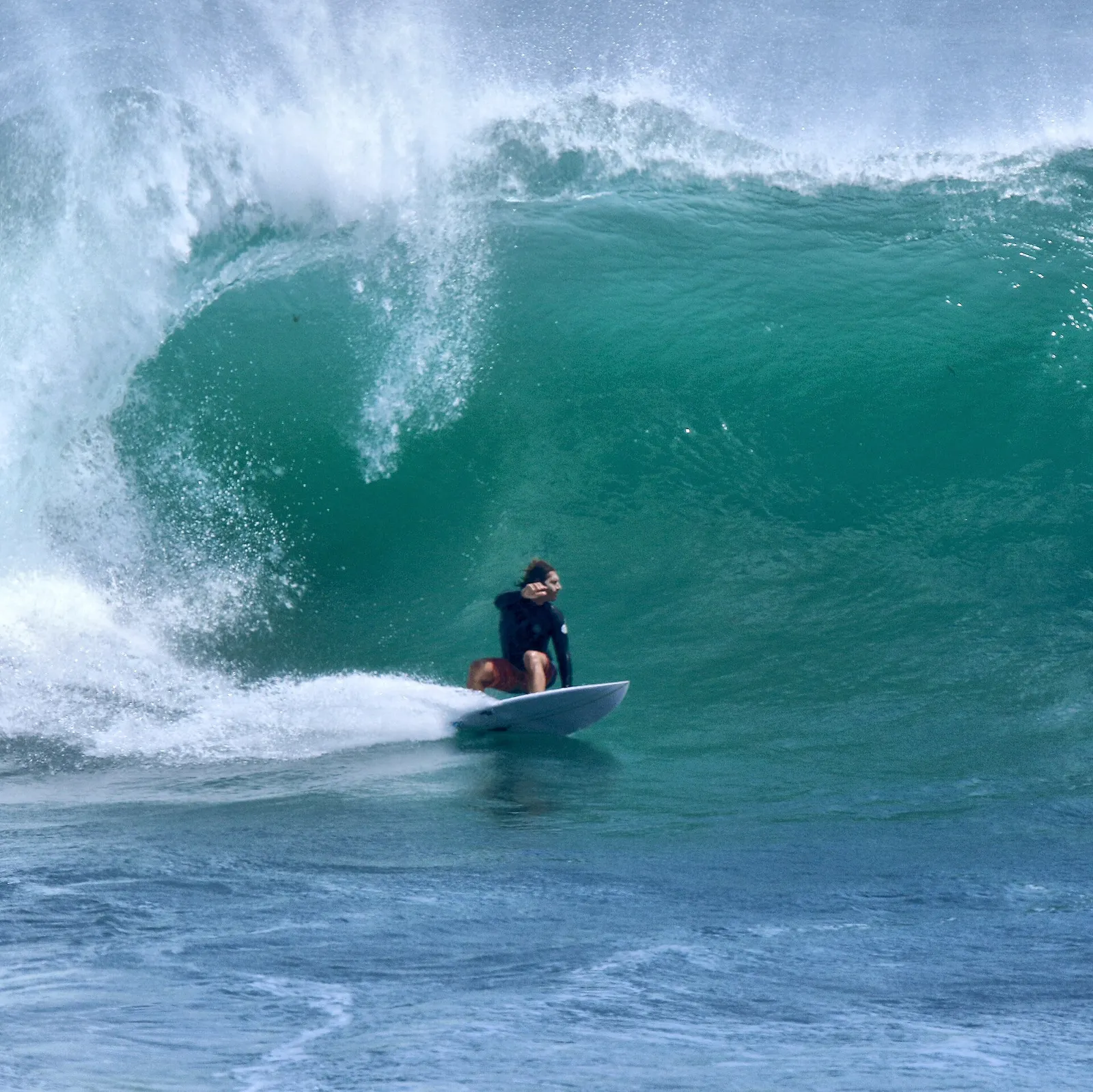 Surfer crouching under the lip of a large turquoise barreling wave