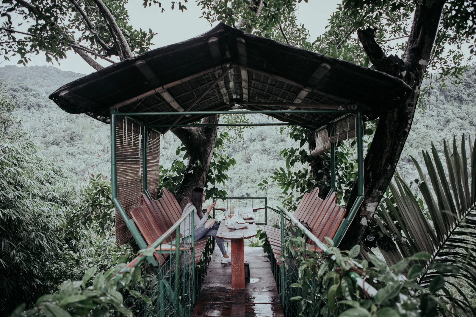 An open sided wooden pavilion with bench seating overlooking dense jungle greenery in Bali