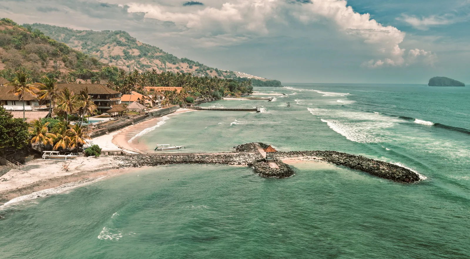A calm shallow lagoon with a paved seafront path and palm trees on the east coast of Bali, Indonesia