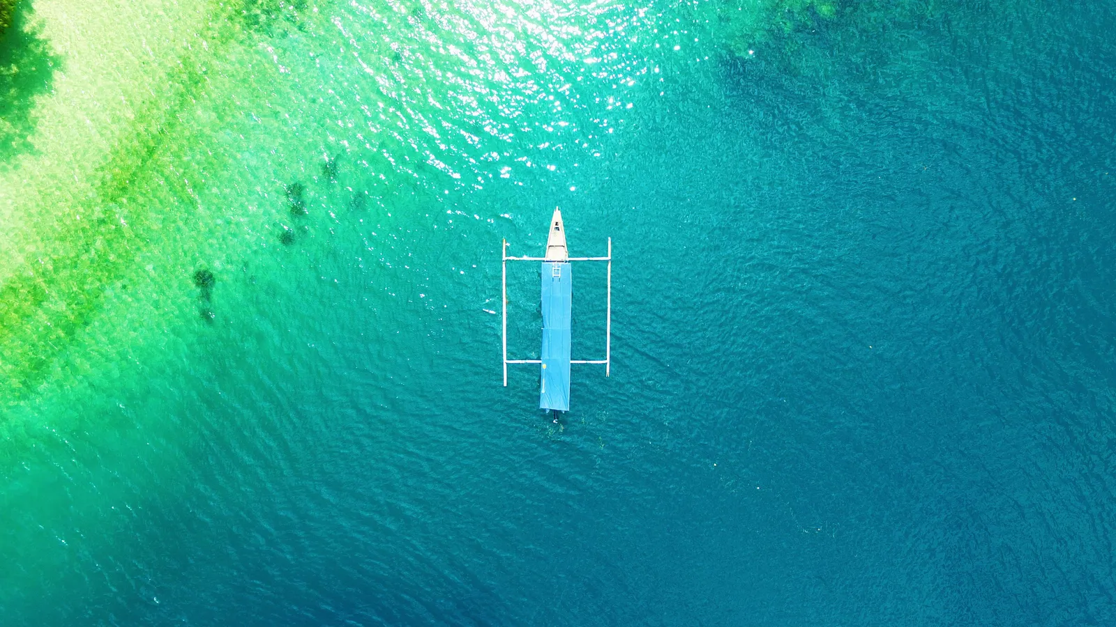 An outrigger fishing boat on the turquoise shallow water off the Gili Islands, seen from above