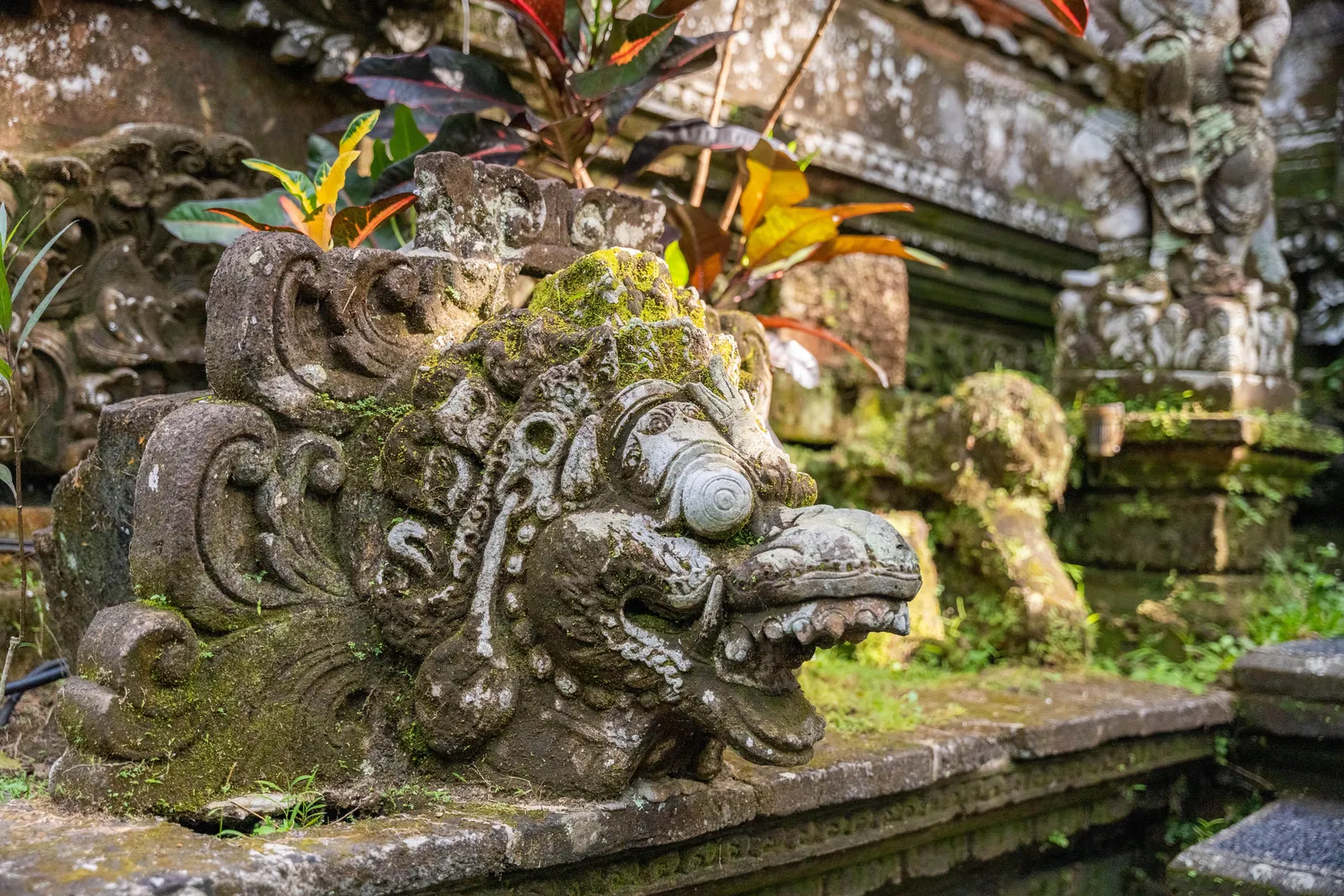 A carved Balinese stone spout beside a bathing pool in a mossy green garden