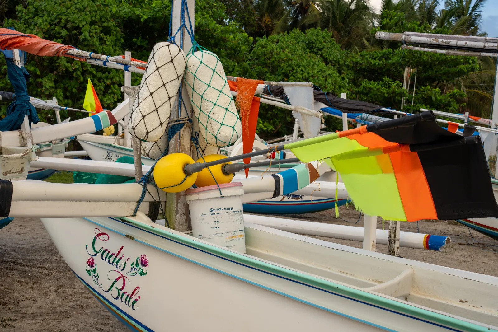 Traditional Balinese outrigger fishing boats pulled up on the sand with their flags and floats