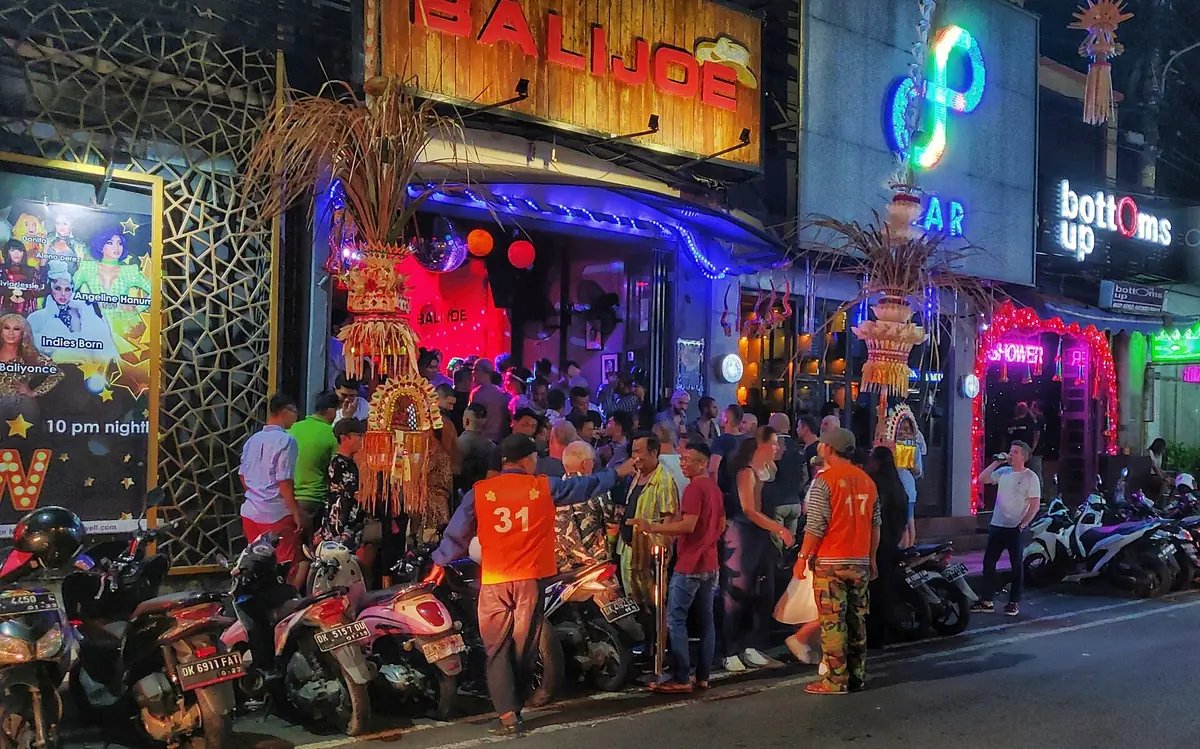 A neon lit bar street with a crowd in the evening