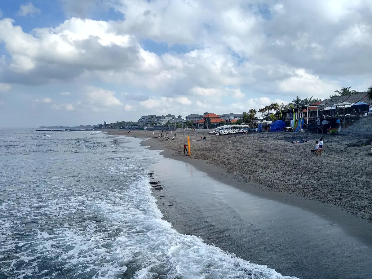 A dark sand beach with parasols and breaking waves