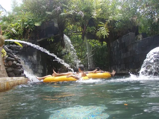 Yellow inner tubes drifting along a slow water channel between artificial waterfalls and greenery