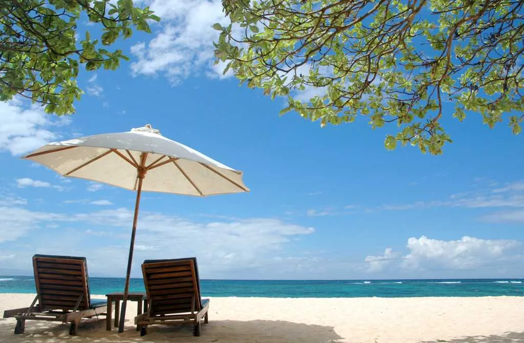 A white parasol and two sun loungers on white sand facing a turquoise sea