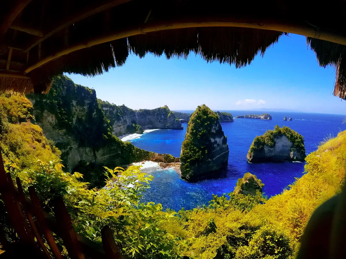 View from inside a thatched hut over green cliffs and small islands in deep blue sea