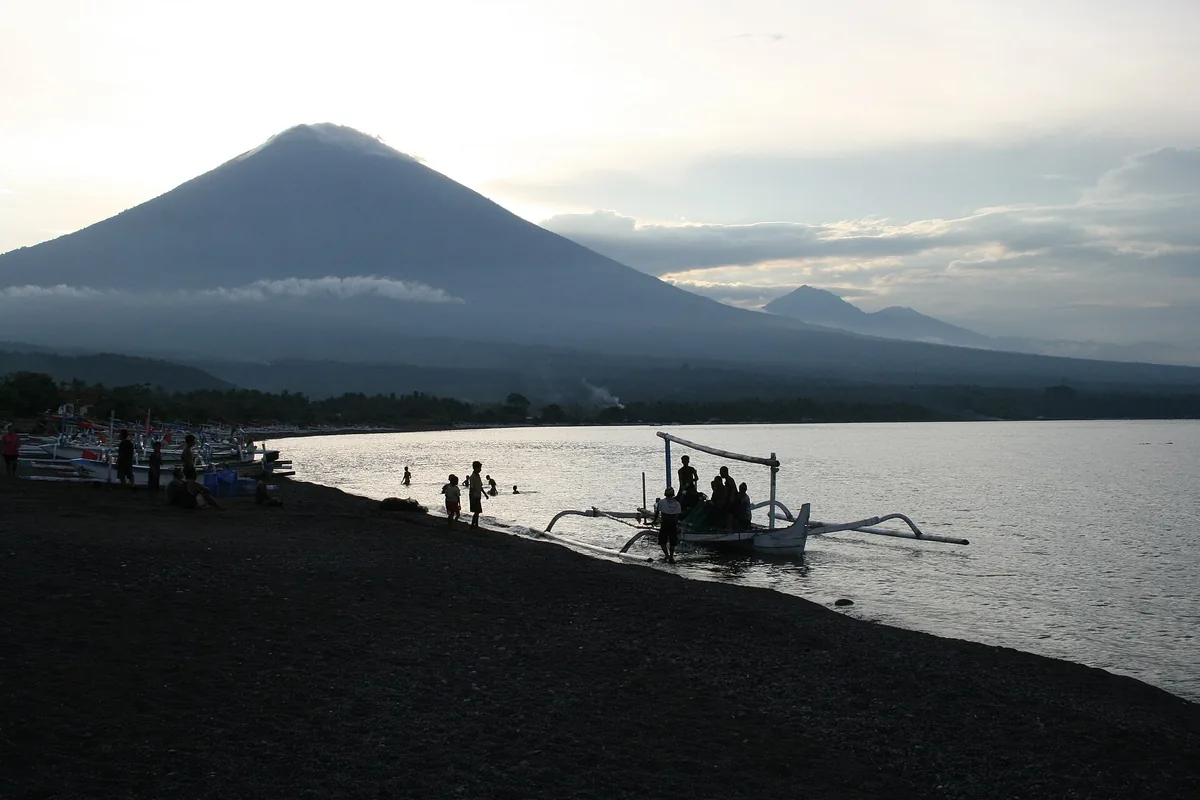 A dark pebble beach with a boat and a volcano silhouette at sunset