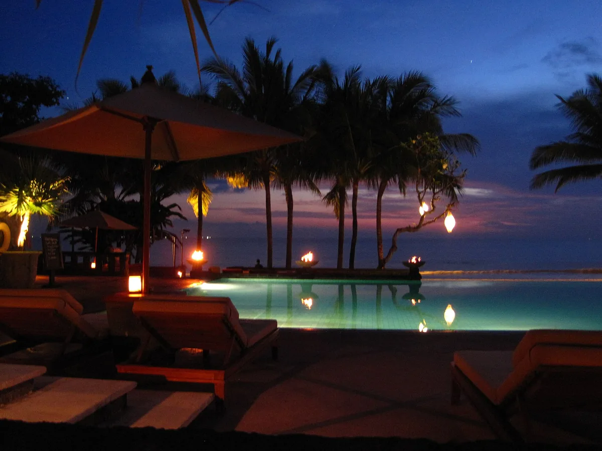 A beachfront terrace with a parasol and lanterns at dusk
