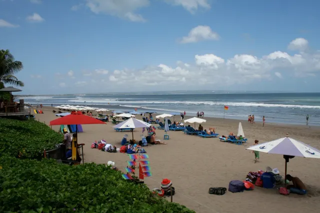 A wide sandy shore with colourful umbrellas, sun loungers and visitors facing the sea