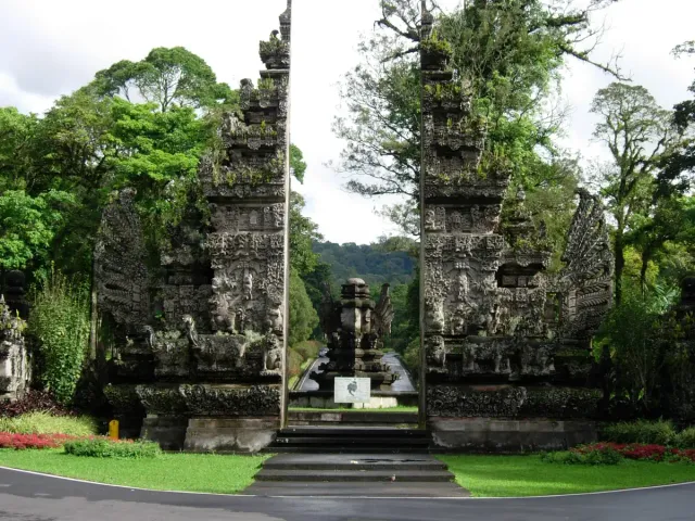 A carved split stone gate on a lawn, with forested hills behind