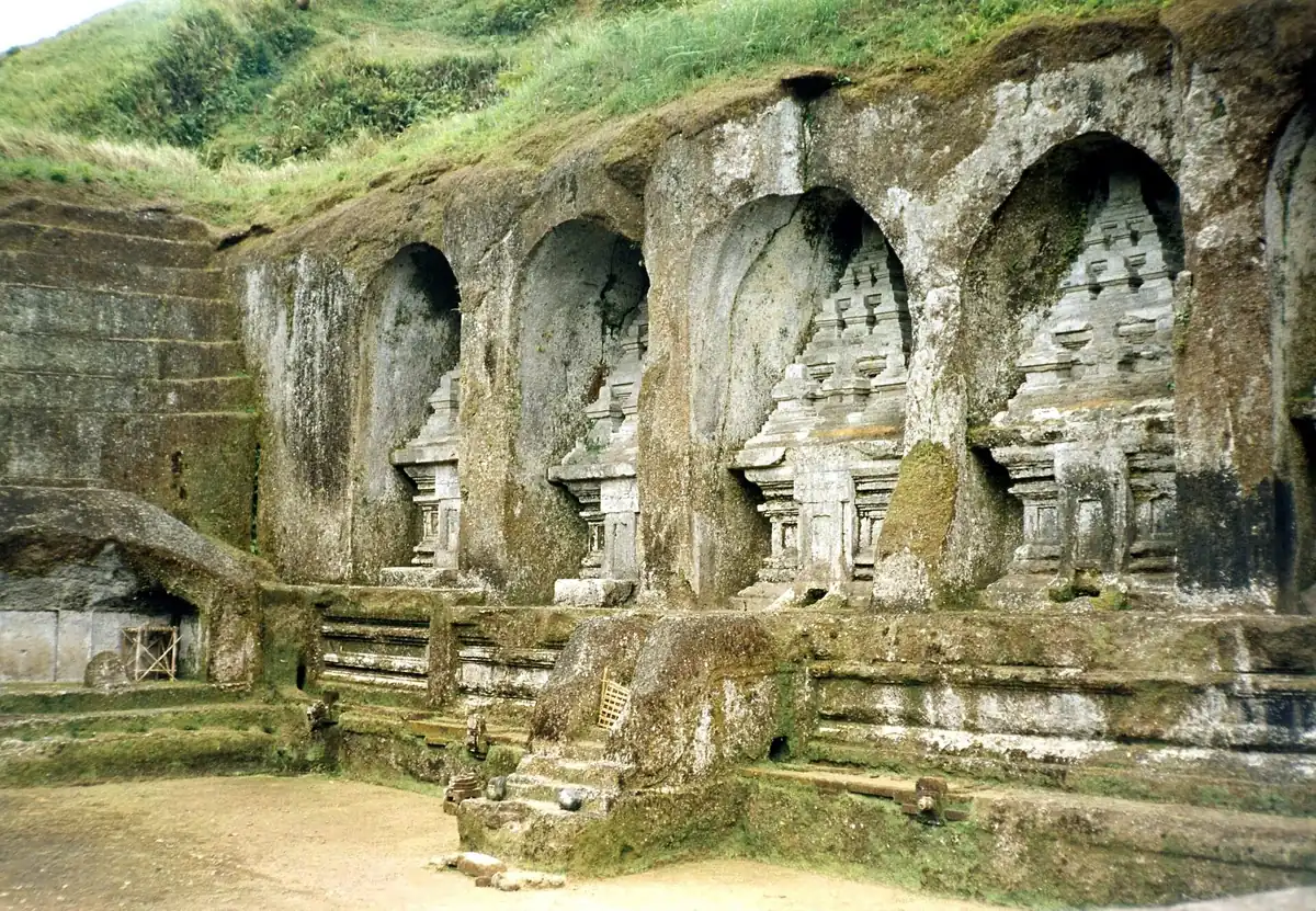 Shrines carved into a tall stone cliff face surrounded by greenery