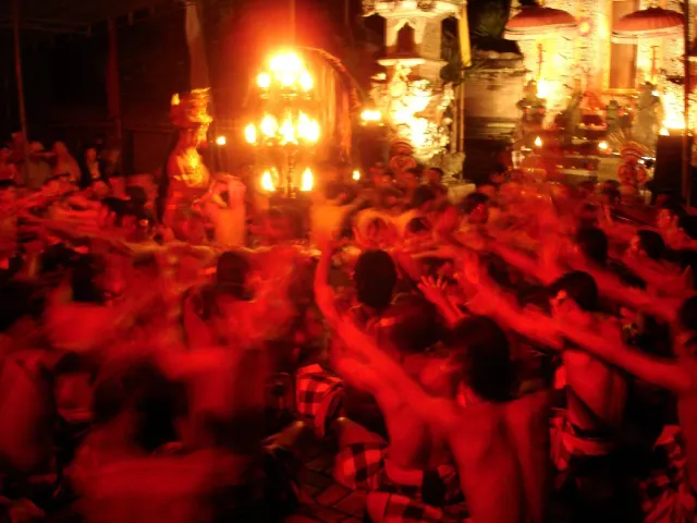 A circle of bare chested dancers with raised arms around a lit candle stand at night