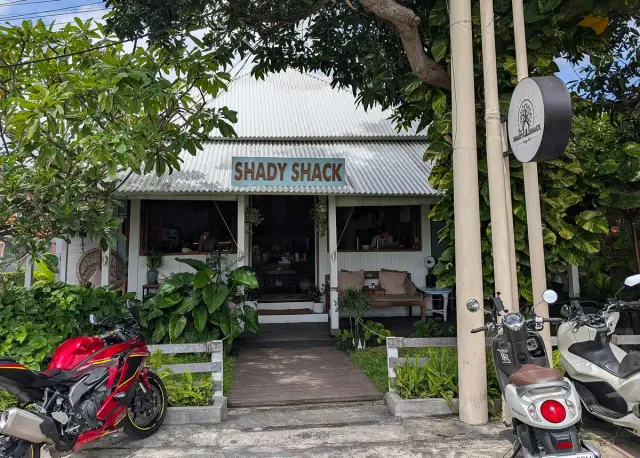 A cafe front with a tin roof and a wooden sign, a bench and plants at the entrance and scooters parked outside
