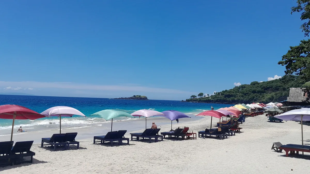 A row of colourful parasols and sun loungers on white sand beside blue water