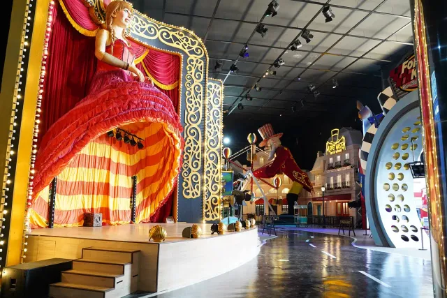 A covered indoor street in an amusement park, with a lit stage in red curtains and gold trim
