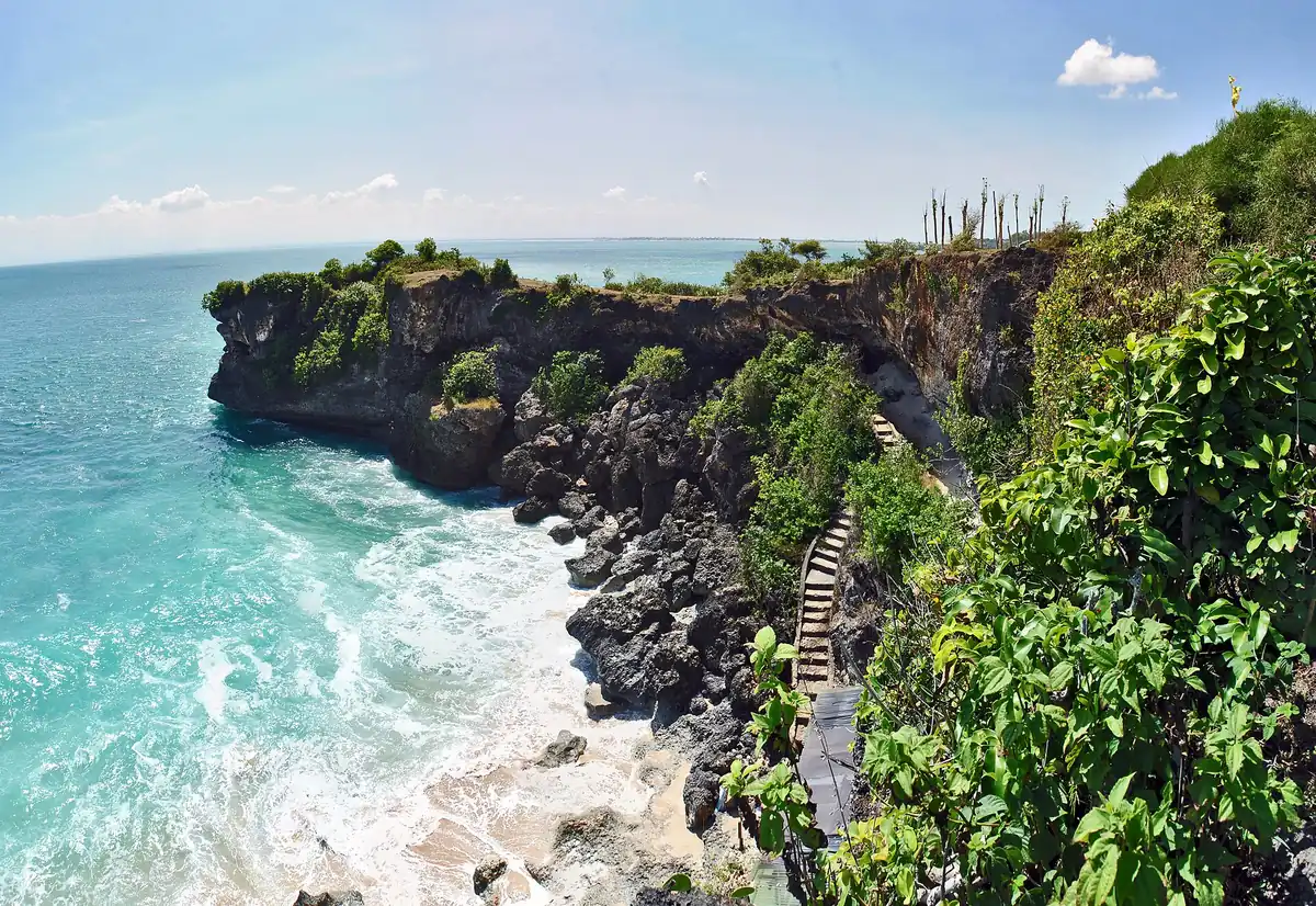 Turquoise water and wooden steps descending between dark rocks to a strip of sand