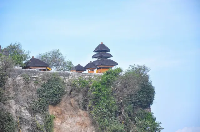 A small temple at the edge of a steep cliff above the ocean, surrounded by greenery