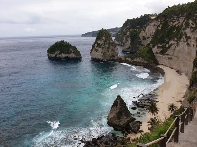 A bay with white limestone cliffs, pale sand and turquoise water, a lone rock standing offshore