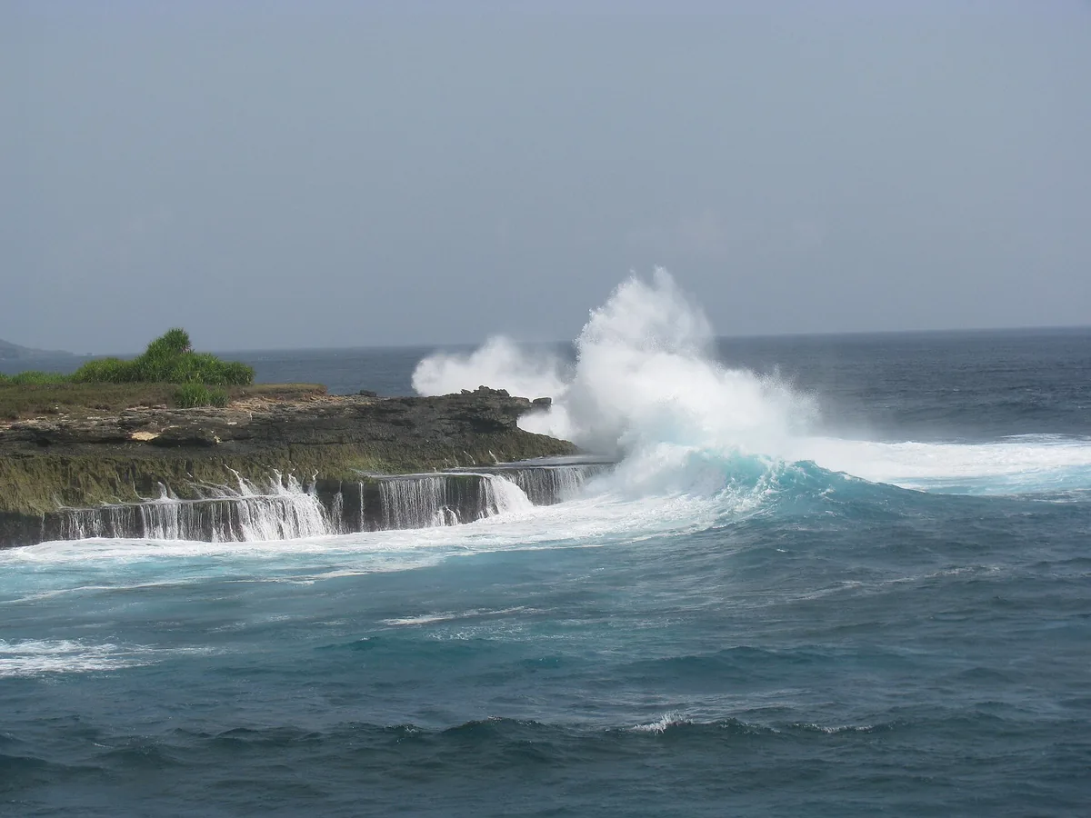 A wave bursting against a rock shelf and throwing up a column of white spray