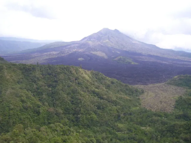 A dark volcanic cone above a black lava field and green hills