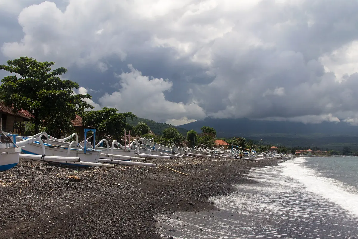 A grey sand beach with boats and hills behind