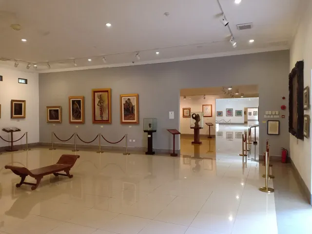 A lit gallery hall with framed paintings on pale walls and a marble floor