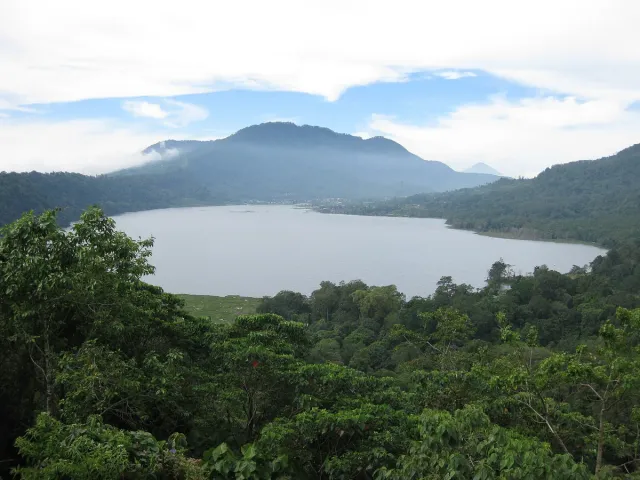 A still lake ringed by forested hills with light mist above the water