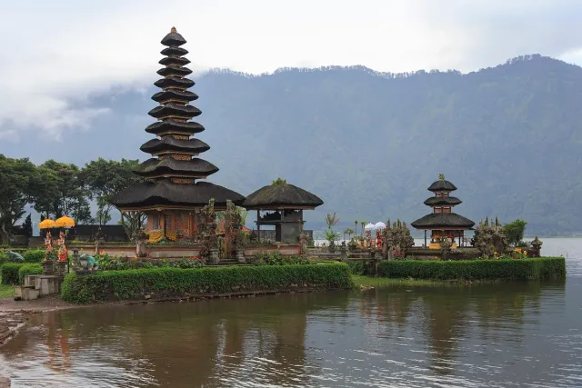 A temple with stacked thatched roofs standing on a small island in a lake, mountains behind