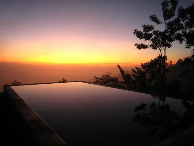 An infinity pool at the edge of a slope, with an open view over a sea of clouds at sunrise