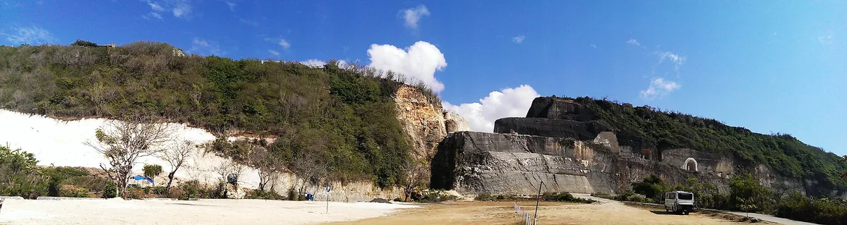 Tall limestone cliffs cut into steps, with a narrow strip of sand and blue water below