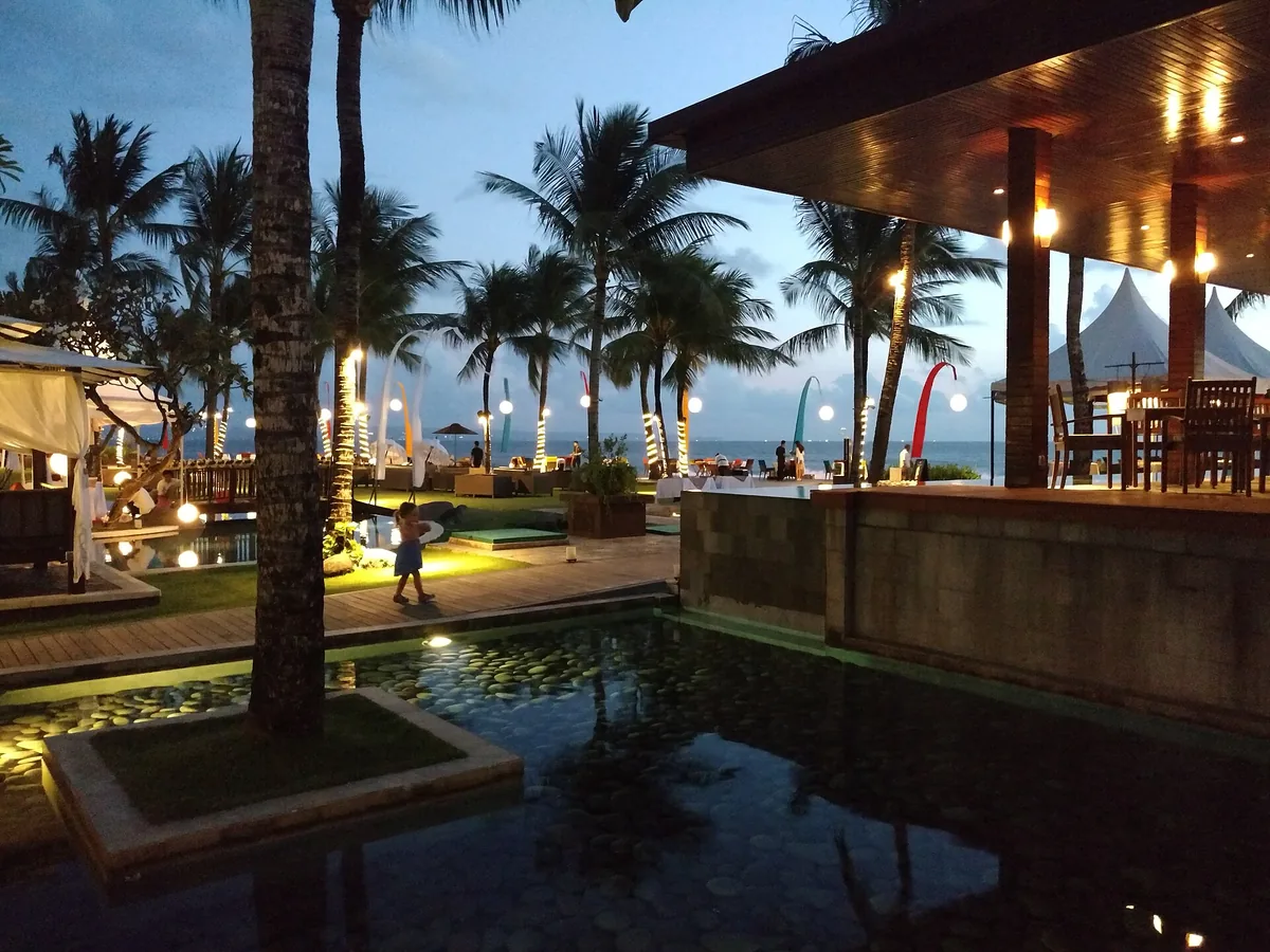 A lit beachfront restaurant among palms at dusk