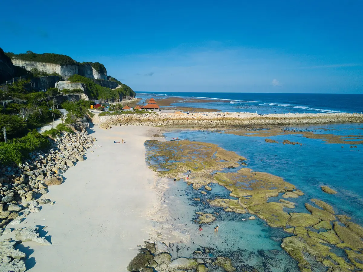 White sand between limestone cliffs and turquoise reef pools, seen from above