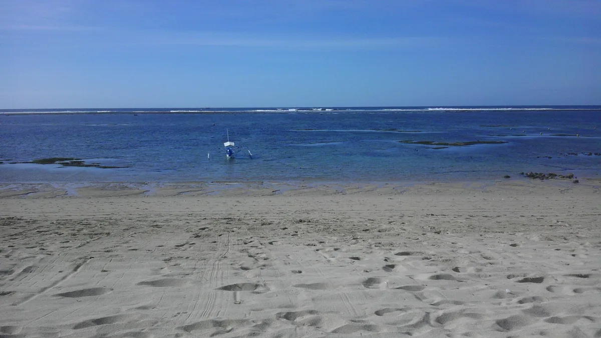 A wide beach with shallow water and a reef line