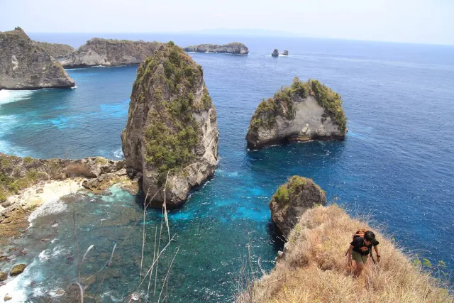 A bay ringed by steep cliffs with rock stacks in turquoise water and white sand below
