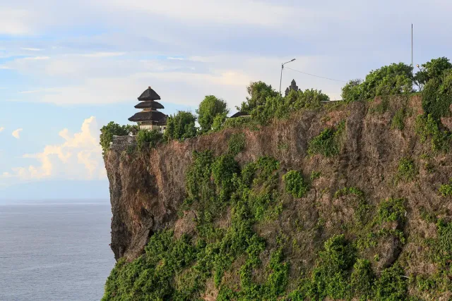 A temple with a stacked roof on the edge of a high limestone cliff dropping straight to the sea