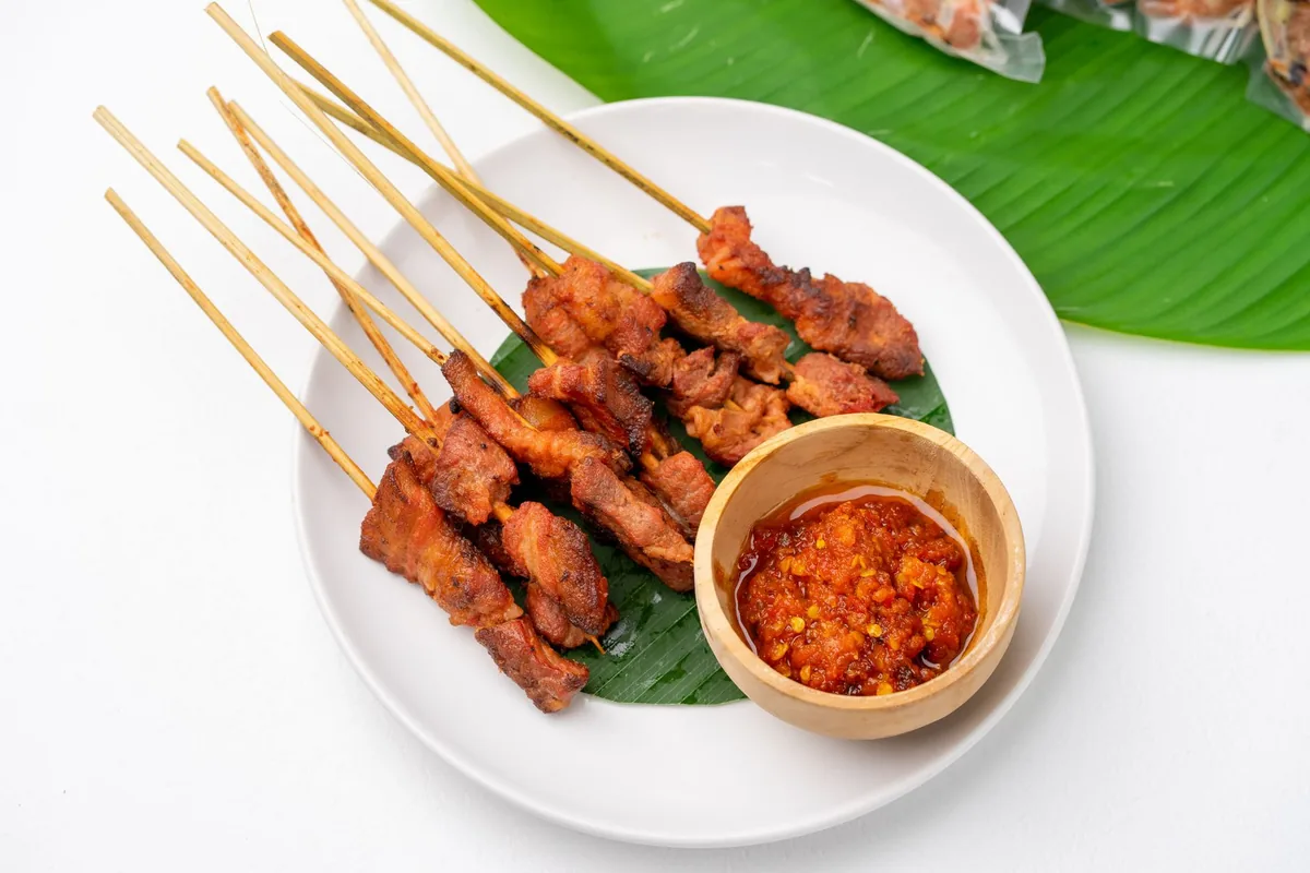 Satay skewers on a banana leaf beside a bowl of sambal