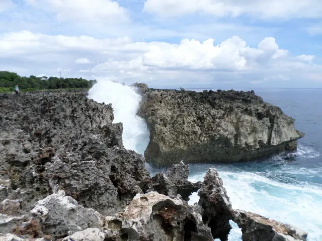 A jet of white spray bursting out of a channel in the limestone shelf at the sea edge