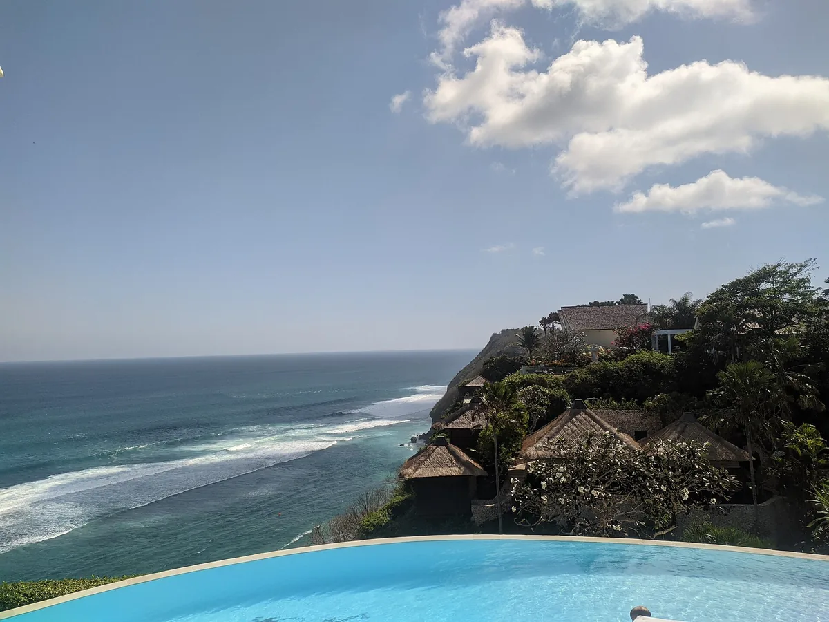A clifftop infinity pool with thatched pavilions above a turquoise sea
