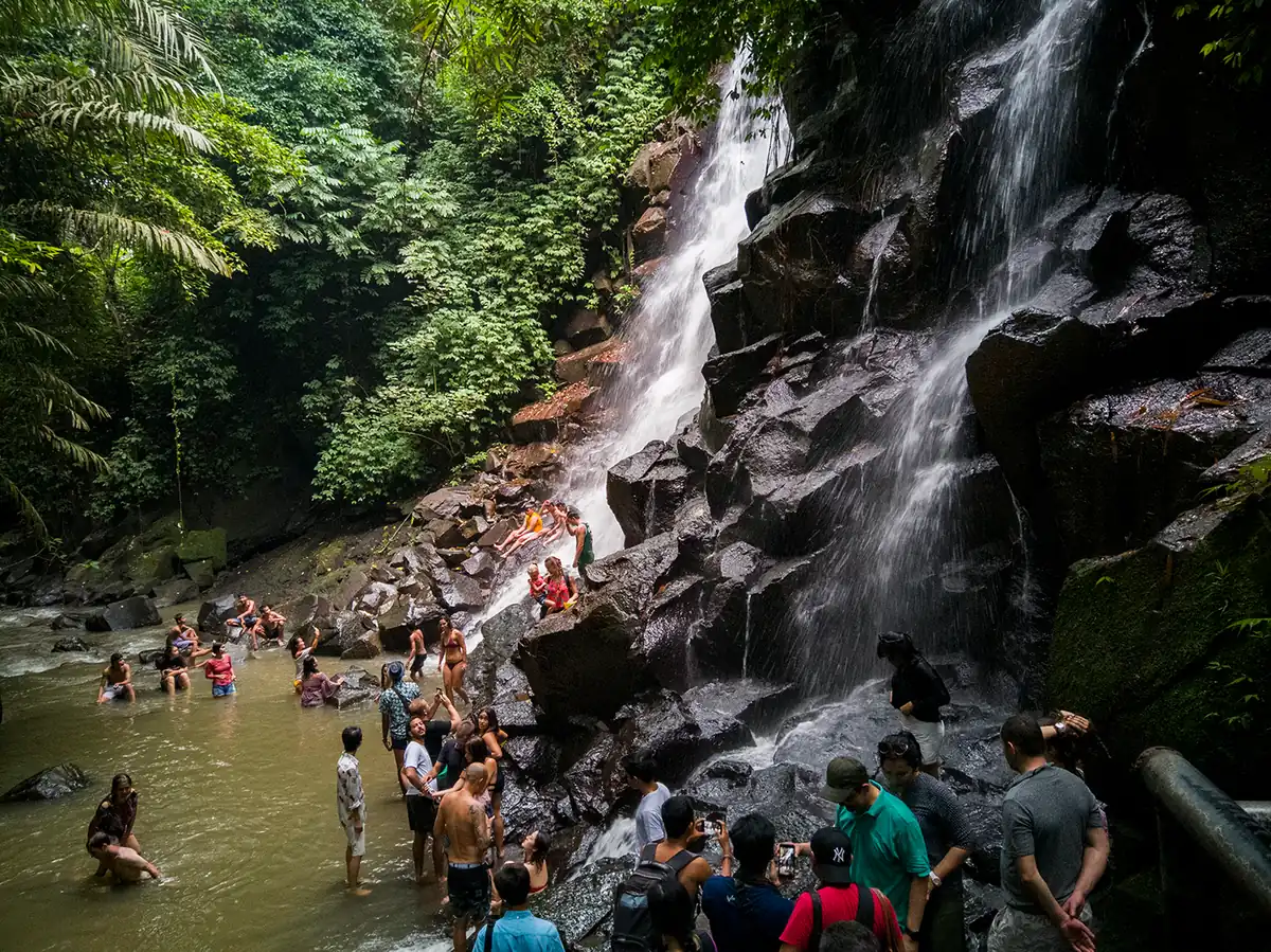 A tiered waterfall over rock with visitors at its foot