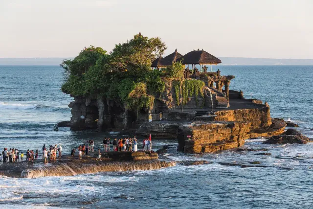 A temple with thatched roofs standing on a rock outcrop in the sea, waves breaking at its base